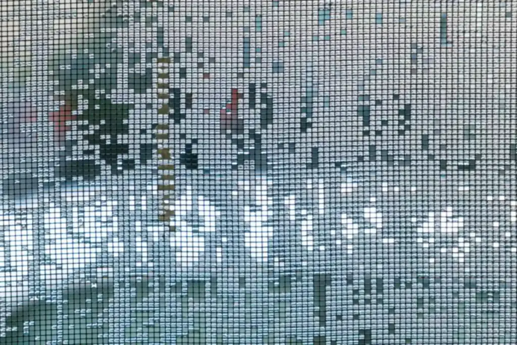 Malla mosquitera de una ventana mojada por la lluvia, vista desde dentro