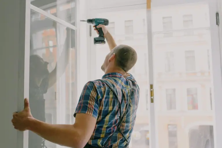 Persona con un taladro trabajando en la parte alta del marco de una ventana